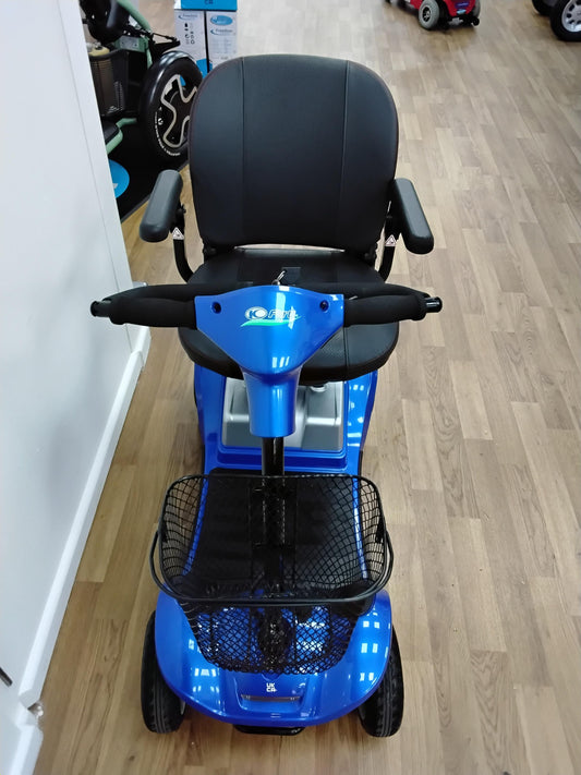 Blue Kymco Mini Comfort mobility scooter with black seat, armrests, and front basket on wooden floor indoors