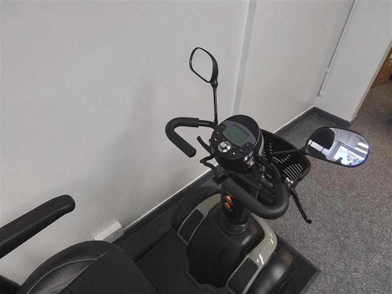 Close-up of the refurbished Excel Evo green scooter dashboard and handlebars with side mirrors indoors on carpet floor.