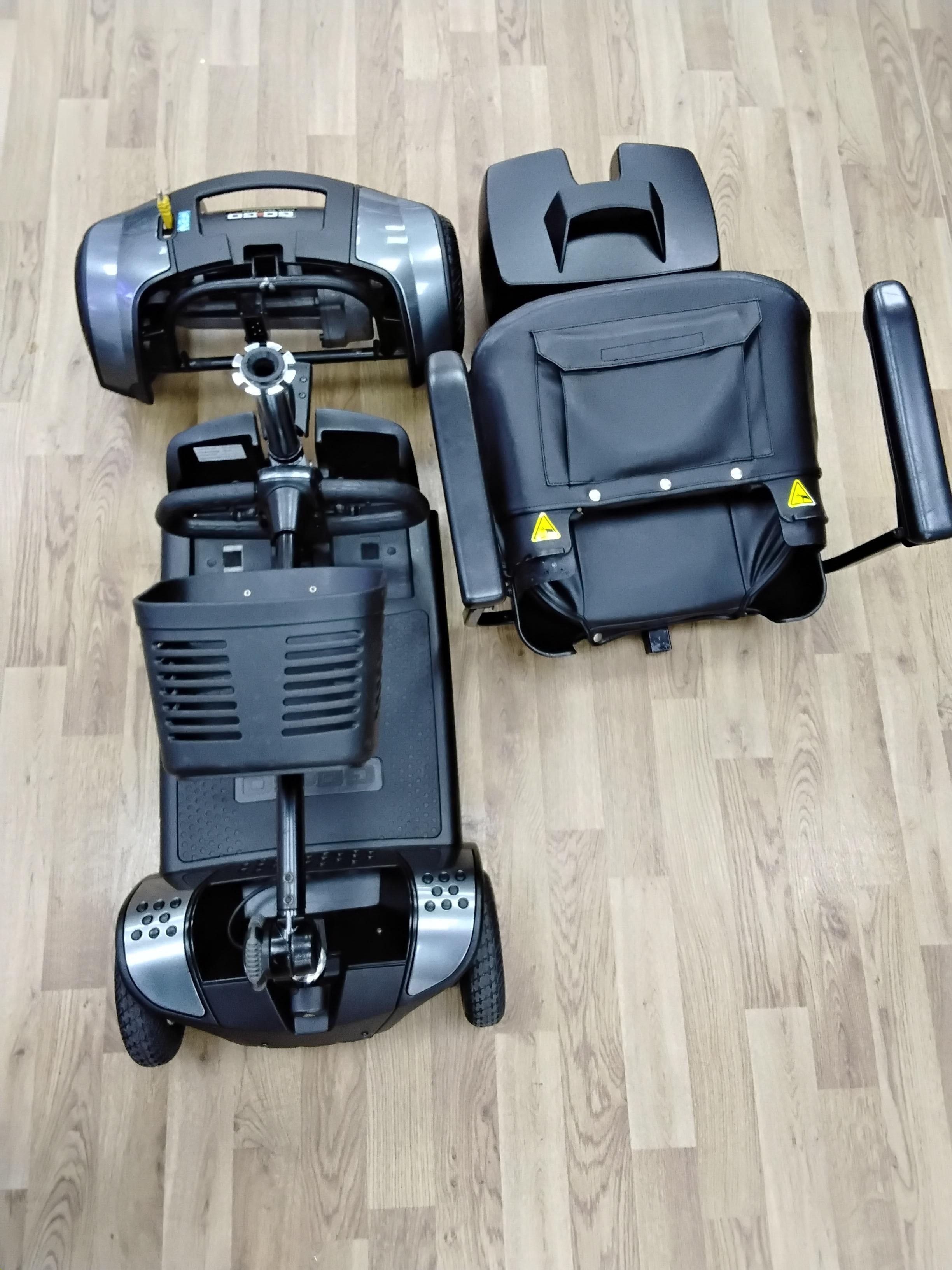Disassembled Pride Go Go Elite Traveller mobility scooter in grey, shown on wooden floor after refurbishment and inspection.