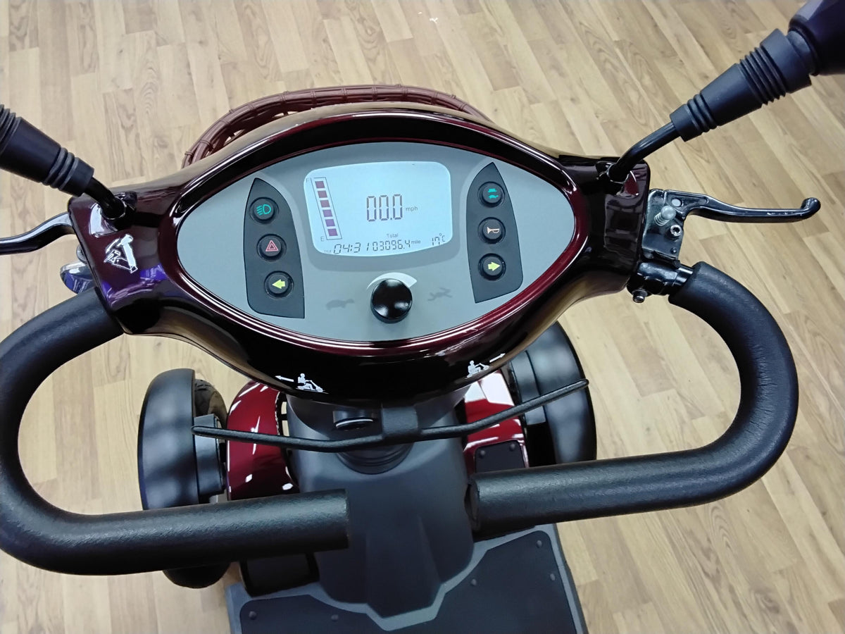Close-up of the maroon Roadmaster Plus R scooter dashboard showing digital display and control buttons on wooden floor background
