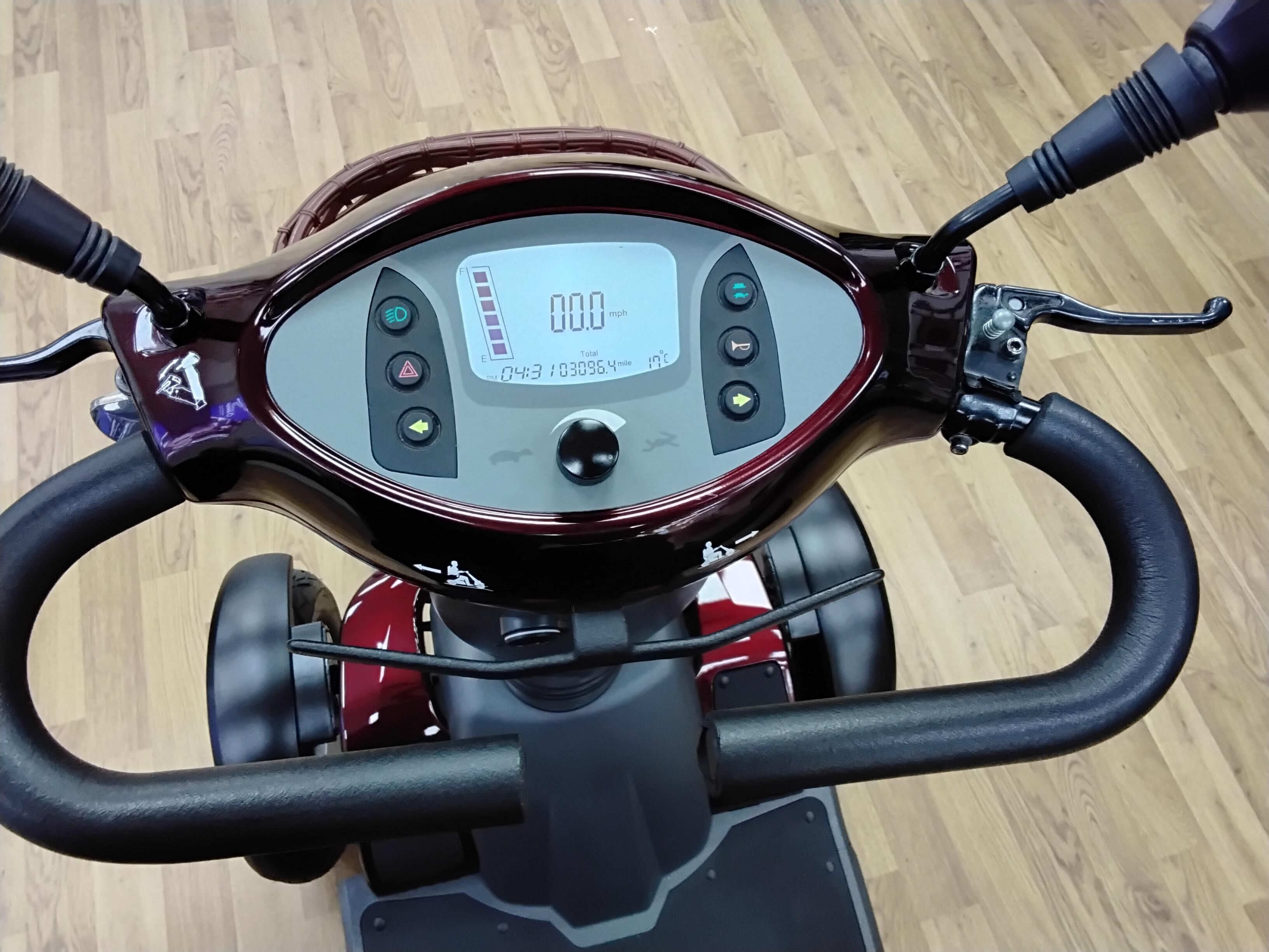 Close-up of the maroon Roadmaster Plus R scooter dashboard showing digital display and control buttons on wooden floor background