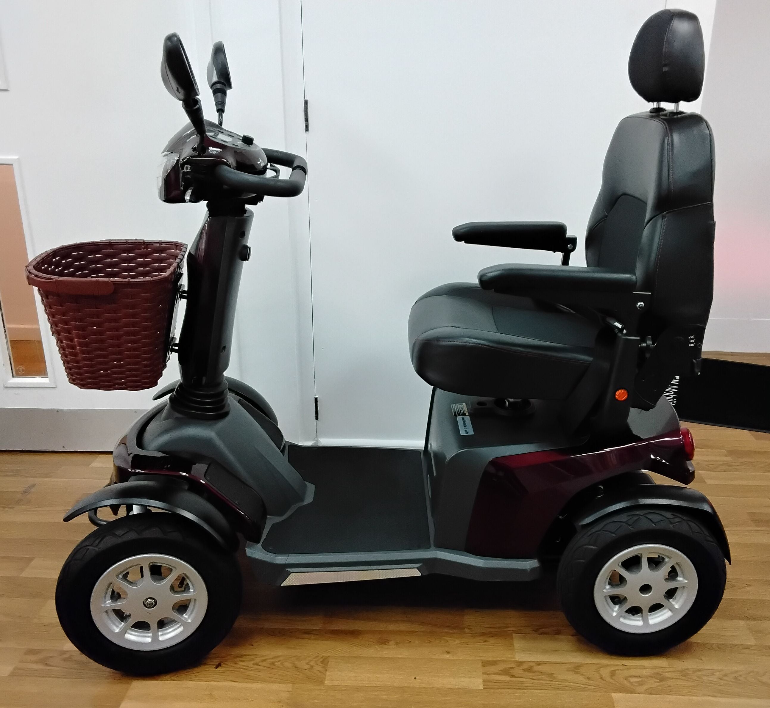 Maroon Roadmaster Plus R mobility scooter with black seat and front basket on wooden floor indoors