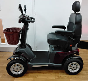 Maroon Roadmaster Plus R mobility scooter with black seat and front basket on wooden floor indoors