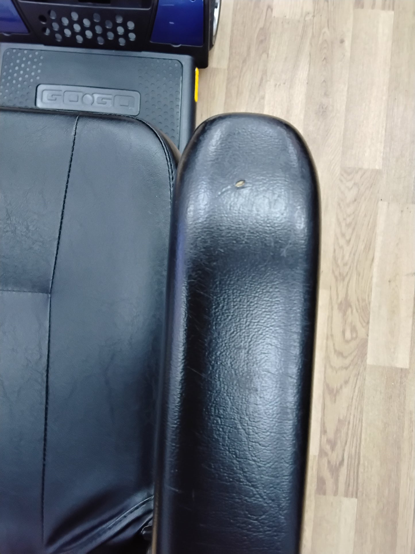 Close-up of black leather armrest and seat of a refurbished Pride Go Go Elite Traveller scooter on wooden floor.