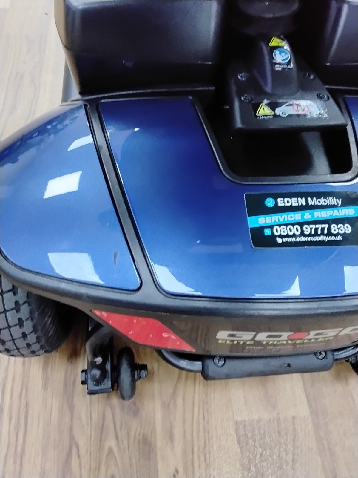 Close-up of the blue Pride Go Go Elite Traveller mobility scooter with Eden Mobility service sticker on wooden floor background