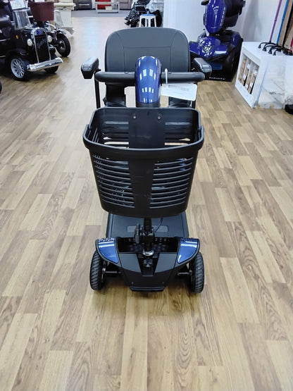Front view of a blue Pride Go Go Elite Traveller mobility scooter with a black basket on a wooden floor indoors