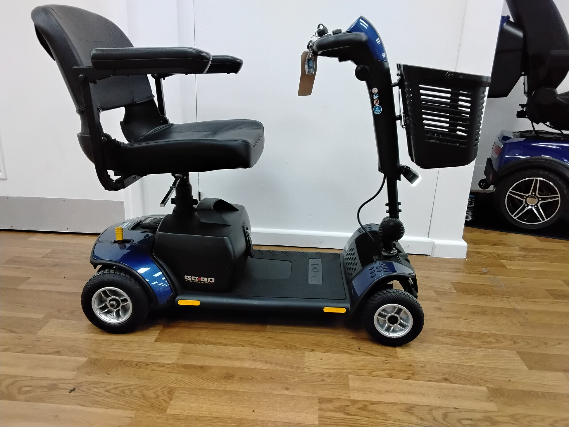 Refurbished blue Pride Go Go Elite Traveller mobility scooter with seat, armrests and front basket on wooden floor.