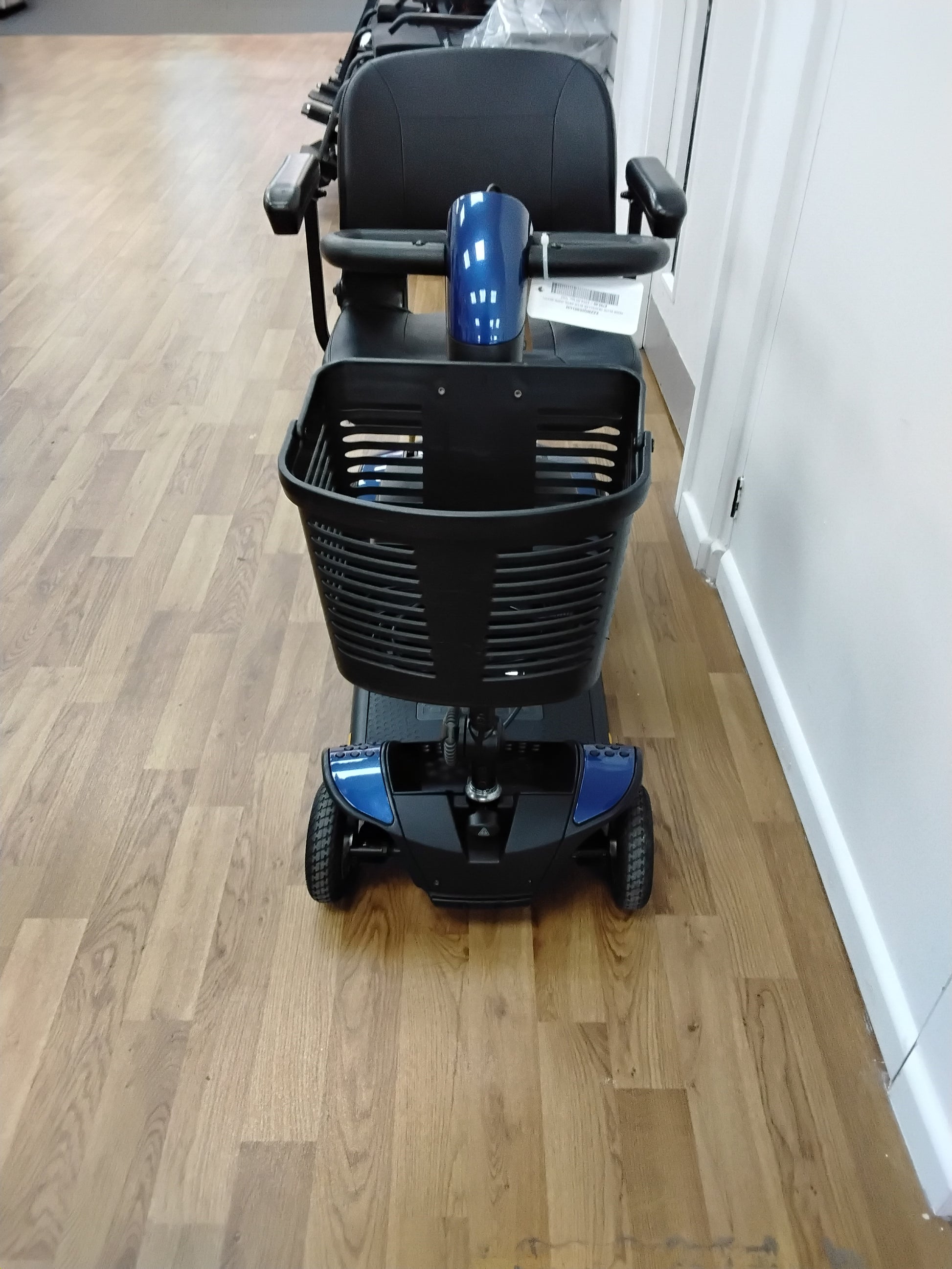 Front view of a refurbished Pride Go Go Elite Traveller mobility scooter with a black basket on wooden floor indoors