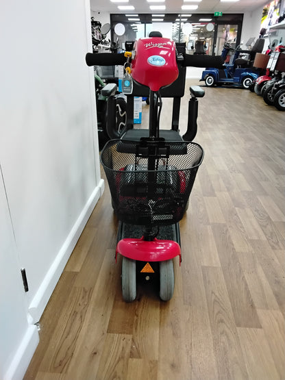 Front view of a red Shoprider Whisper mobility scooter with black basket and handlebars on wooden floor indoors