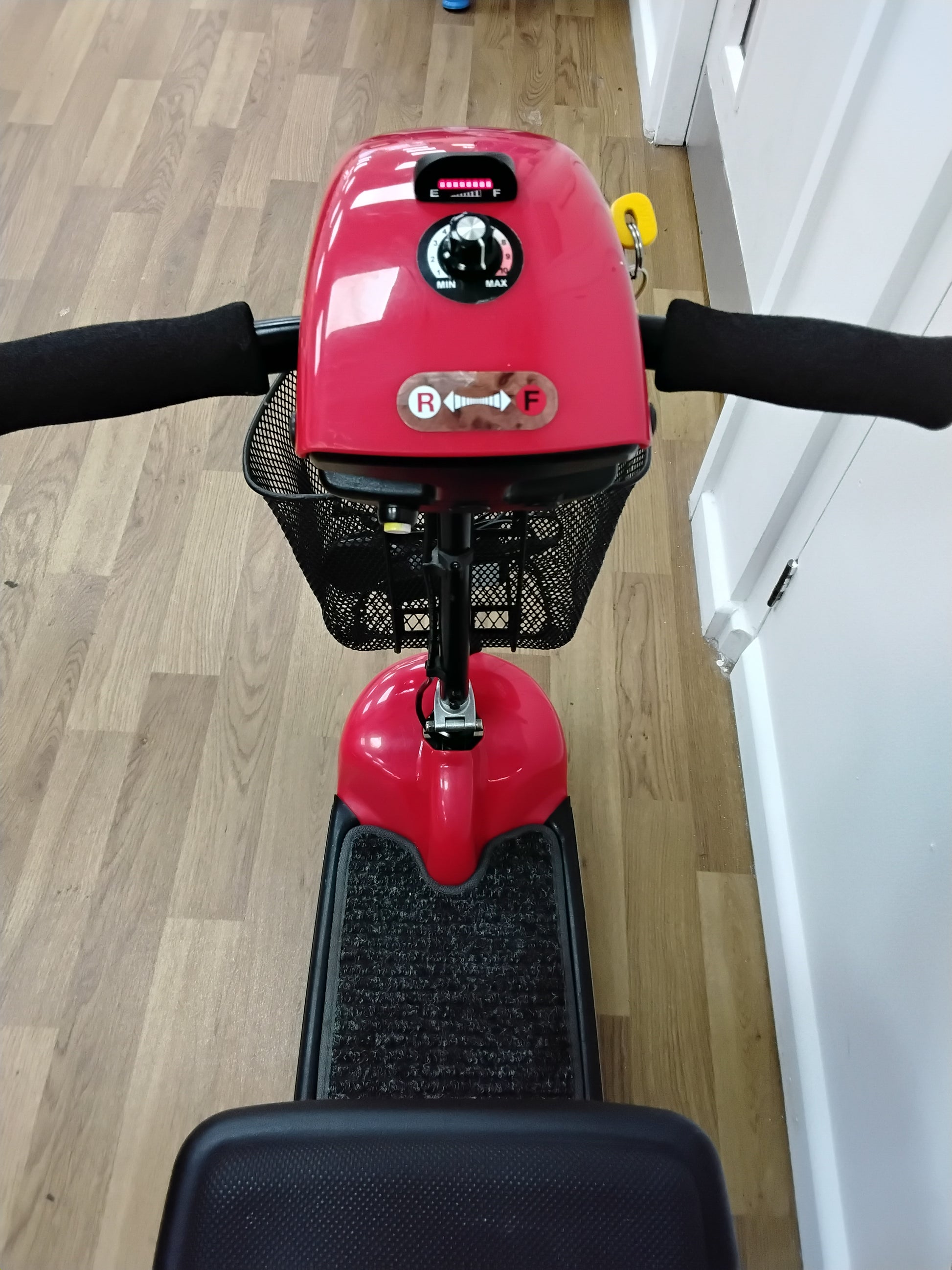 Top view of a refurbished red Shoprider Whisper mobility scooter with black handles and front basket indoors on wooden floor