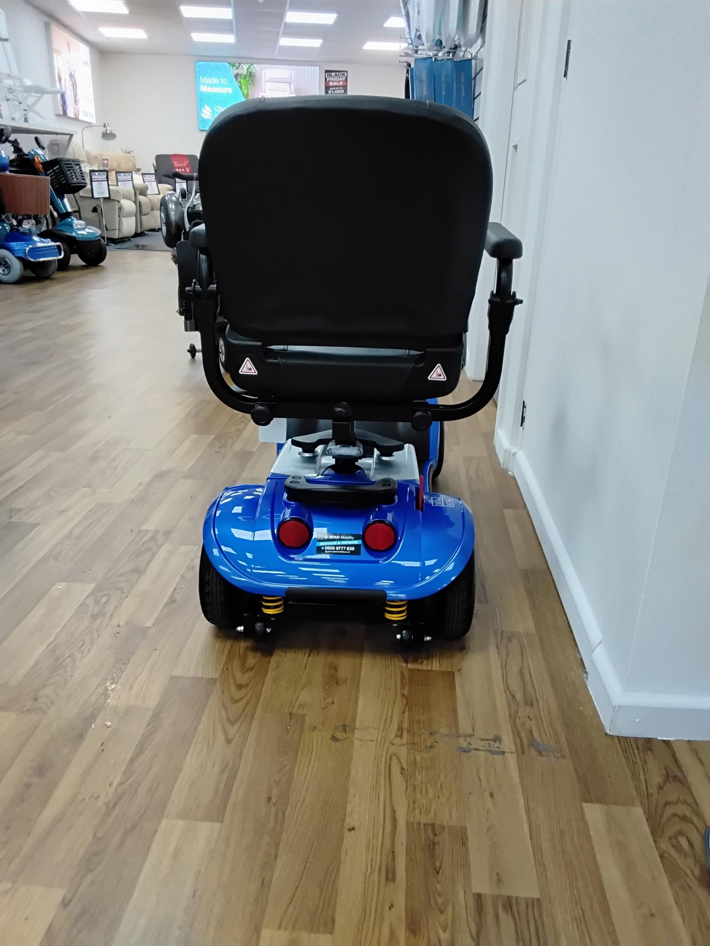 Rear view of a blue Kymco Mini Comfort mobility scooter with black seat and armrests on wooden showroom floor