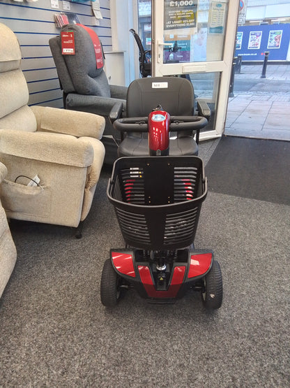 Red Pride Go-Go Elite Traveller mobility scooter with black basket and seat displayed inside a mobility store.