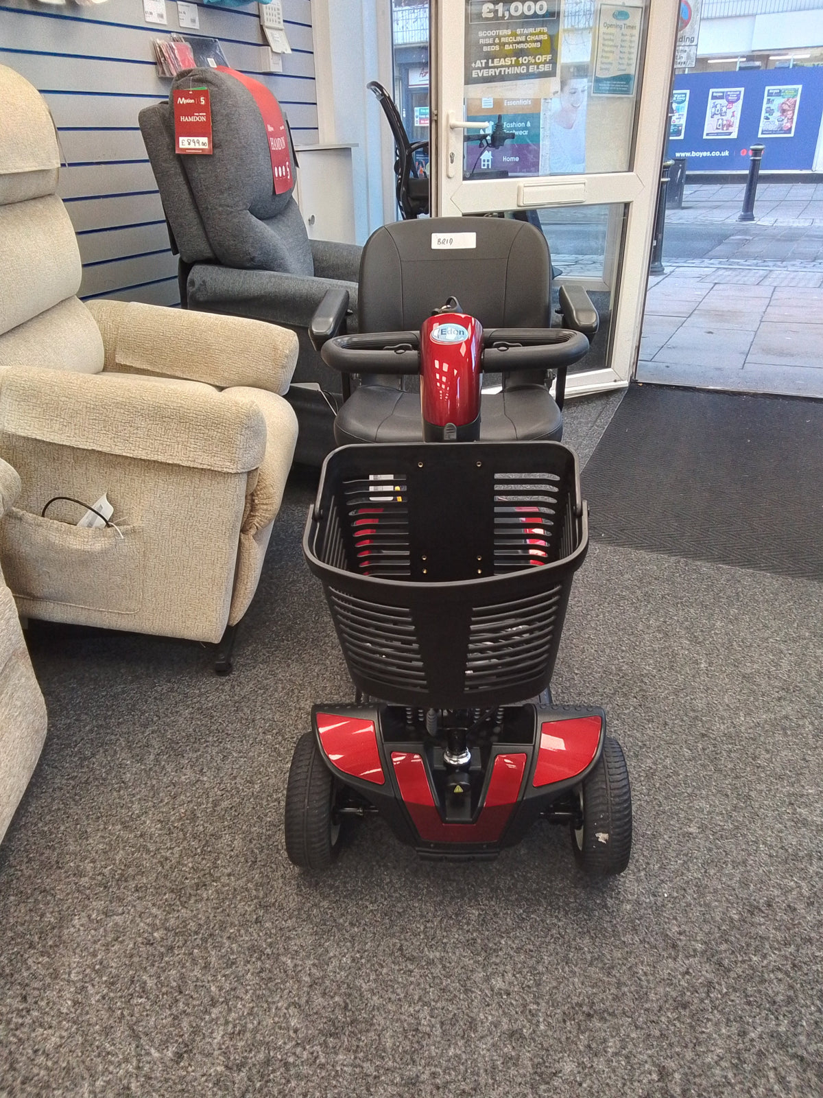 Red Pride Go-Go Elite Traveller mobility scooter with black basket and seat displayed inside a mobility store.