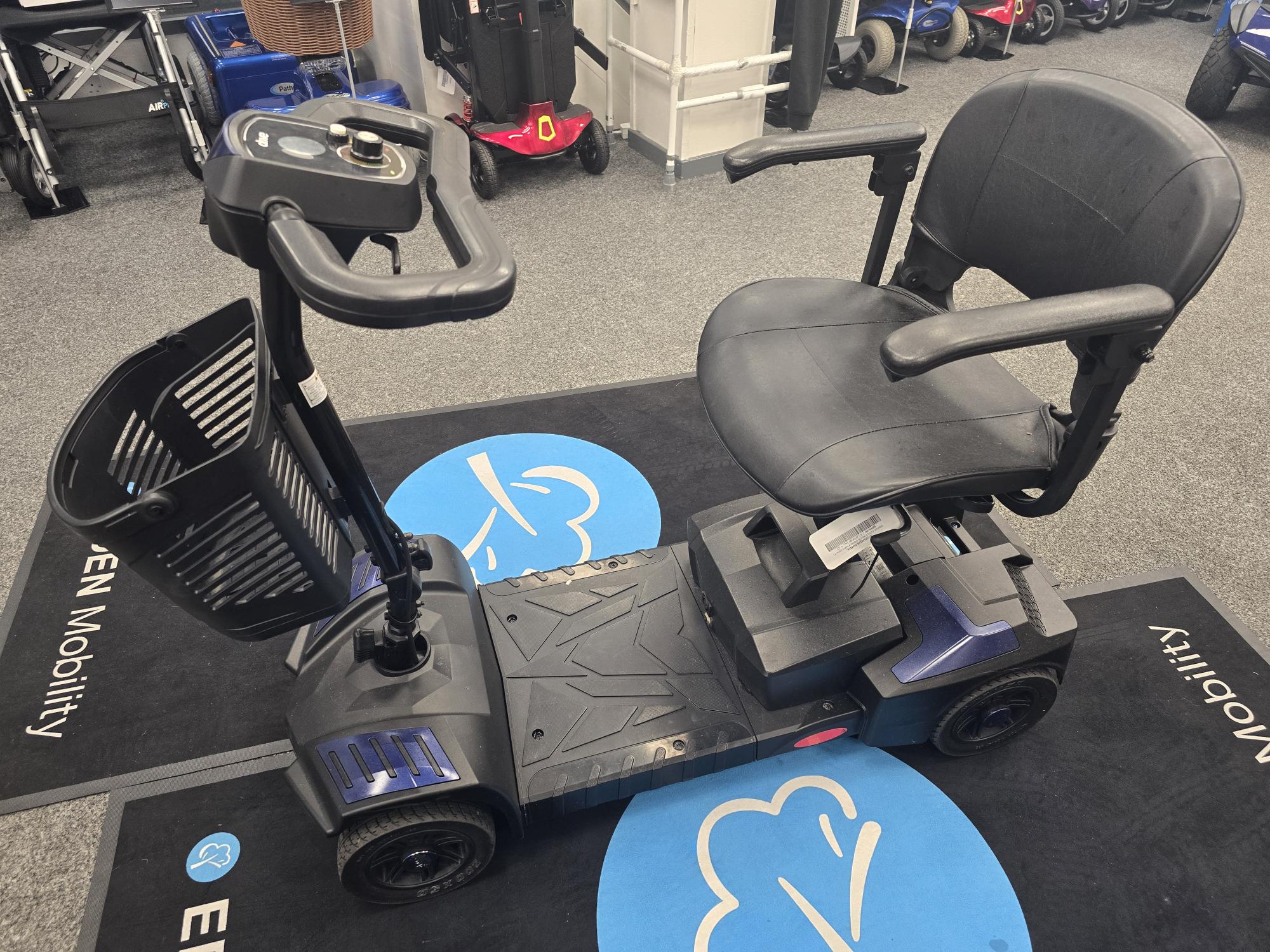 Refurbished Drive Scout Blue mobility scooter with padded seat, armrests, and storage basket on black showroom floor.