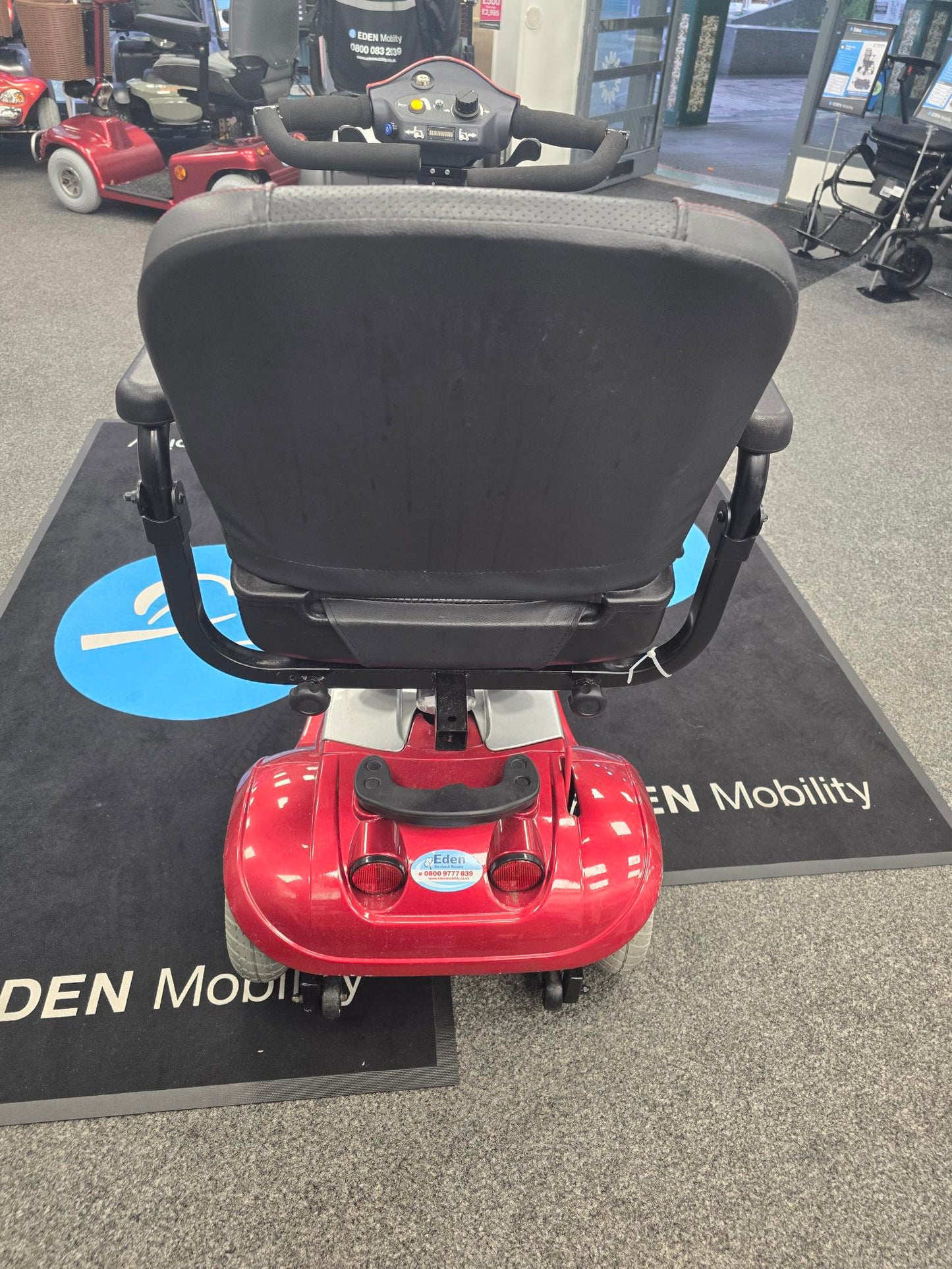 Rear view of a refurbished red Kymco Mini Comfort mobility scooter with black seat and armrests indoors on a showroom floor
