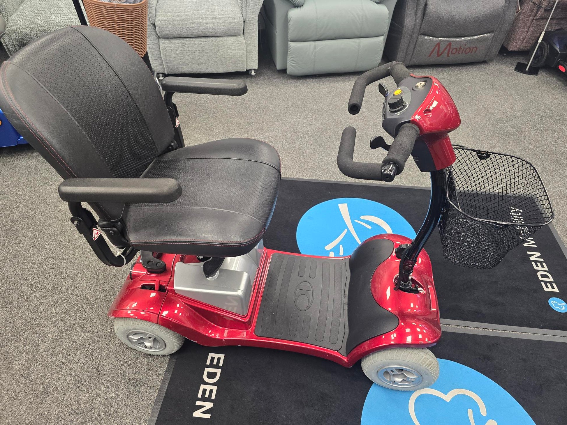 Red Kymco Mini Comfort mobility scooter with black cushioned seat and front basket on gray carpet flooring