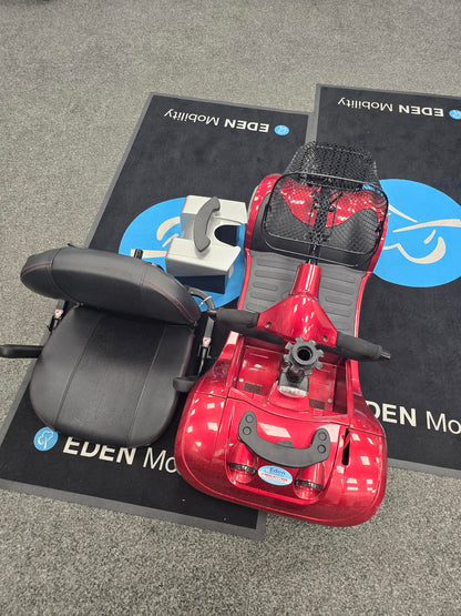 Red Kymco Mini Comfort mobility scooter with detached black seat and basket on an Eden Mobility mat indoors