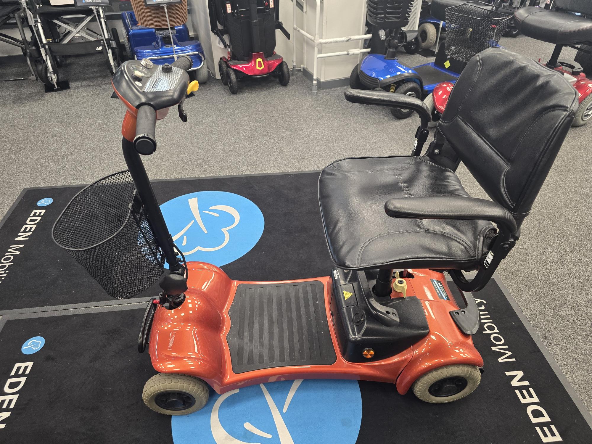 Electric Mobility Ultralite 480 orange refurbished mobility scooter with padded seat and basket on showroom floor