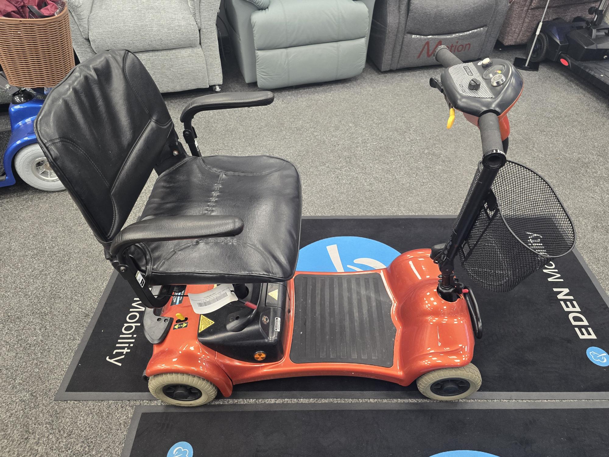 Refurbished Electric Mobility Ultralite 480 orange mobility scooter with black seat and basket on display indoors
