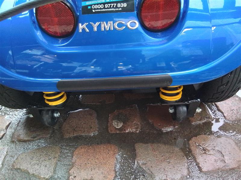 Close-up of rear section of blue Kymco Mini Comfort scooter showing yellow springs and rear wheels on wet cobblestones