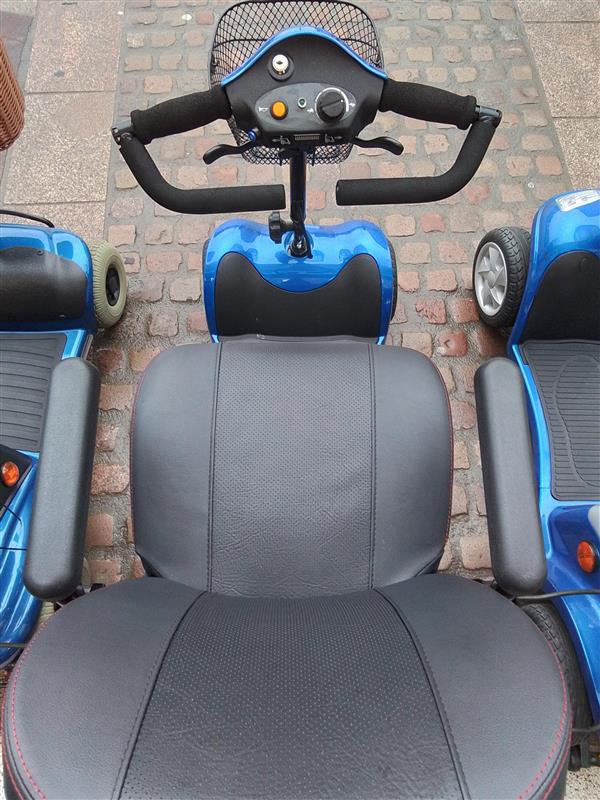 Close-up of black leather seat and handlebars on a blue Kymco Mini Comfort mobility scooter on cobblestone ground