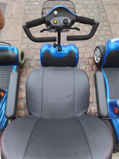 Close-up of black leather seat and handlebars on a blue Kymco Mini Comfort mobility scooter on cobblestone ground