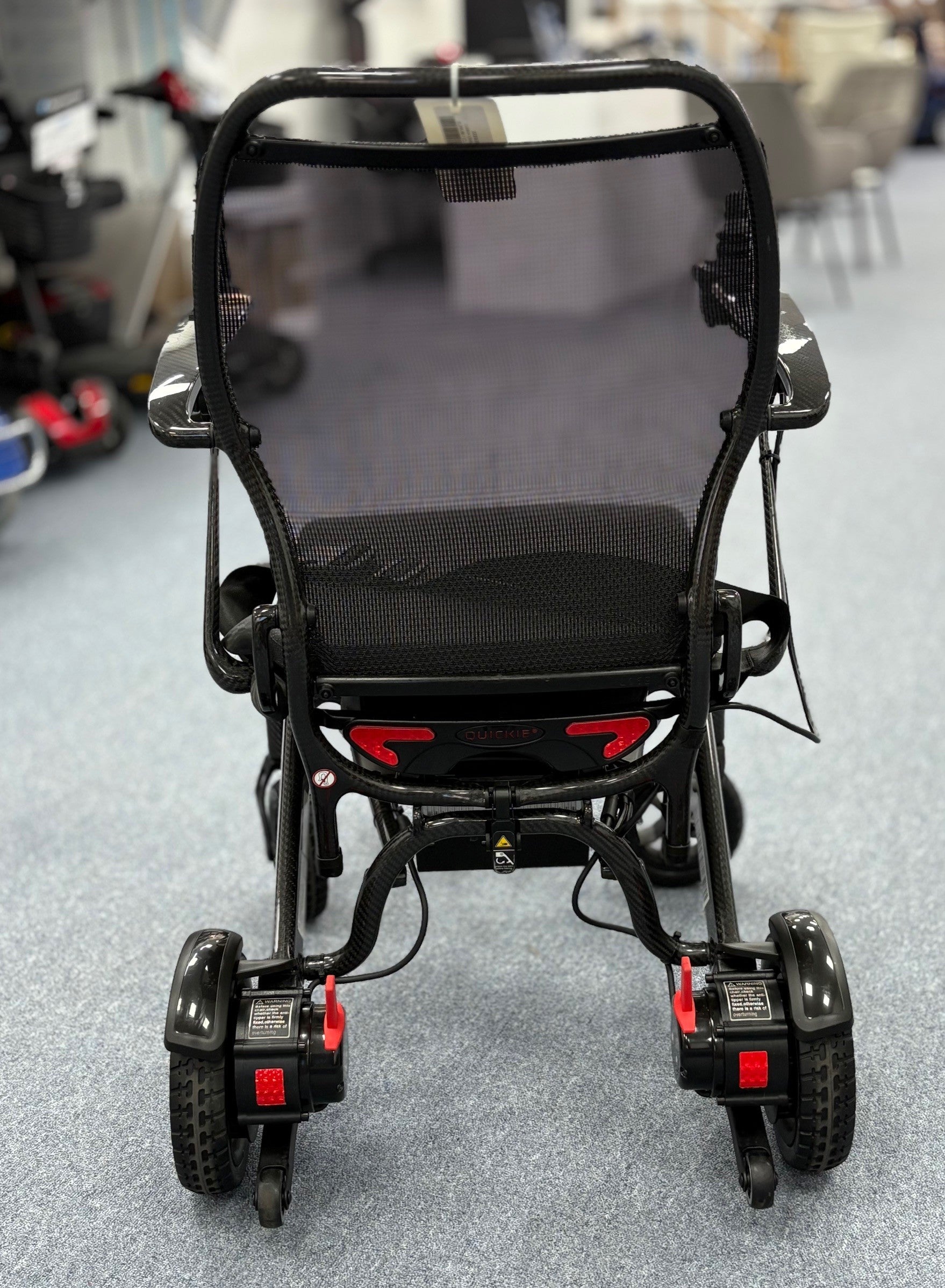 Rear view of a refurbished black Quickie Q50 R Carbon powerchair on a showroom floor with visible rear wheels and frame details