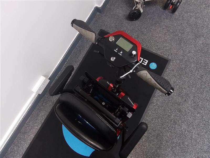 Top view of a refurbished red Drive Auto Fold scooter with padded seat and control panel on a gray carpeted floor