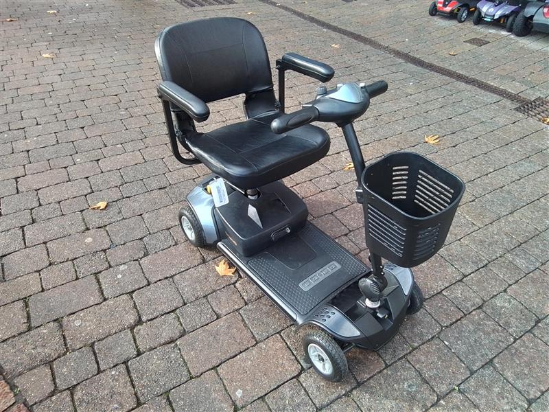 Grey Pride Go Go Elite Traveller mobility scooter with black seat and front basket on brick pavement outdoors
