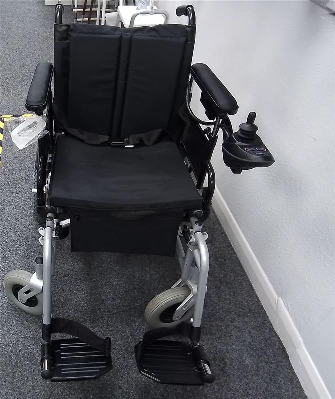 Black and grey powered wheelchair with cushioned seat, armrests, joystick control, and footrests on a gray carpeted floor