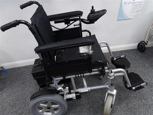 Black and grey Drive Cirrus powerchair with joystick control on gray carpeted floor indoors next to a wall poster