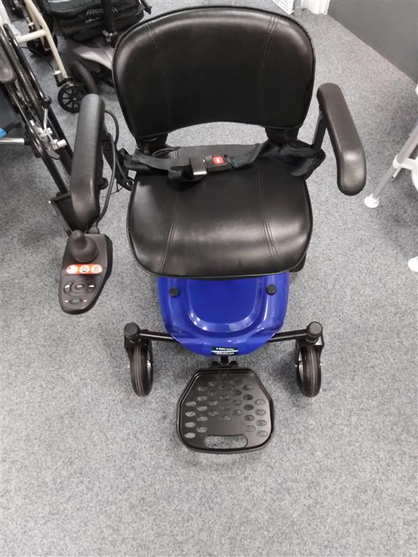 Black leather seat powerchair with armrests, joystick control on left, and blue base on gray carpeted floor