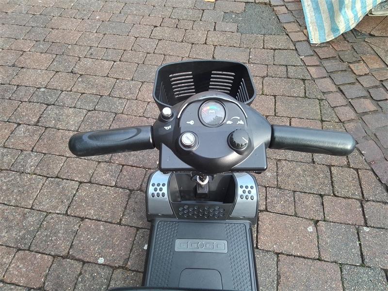 Top view of refurbished grey Pride Go Go Elite Traveller mobility scooter handlebars and control panel on brick pavement