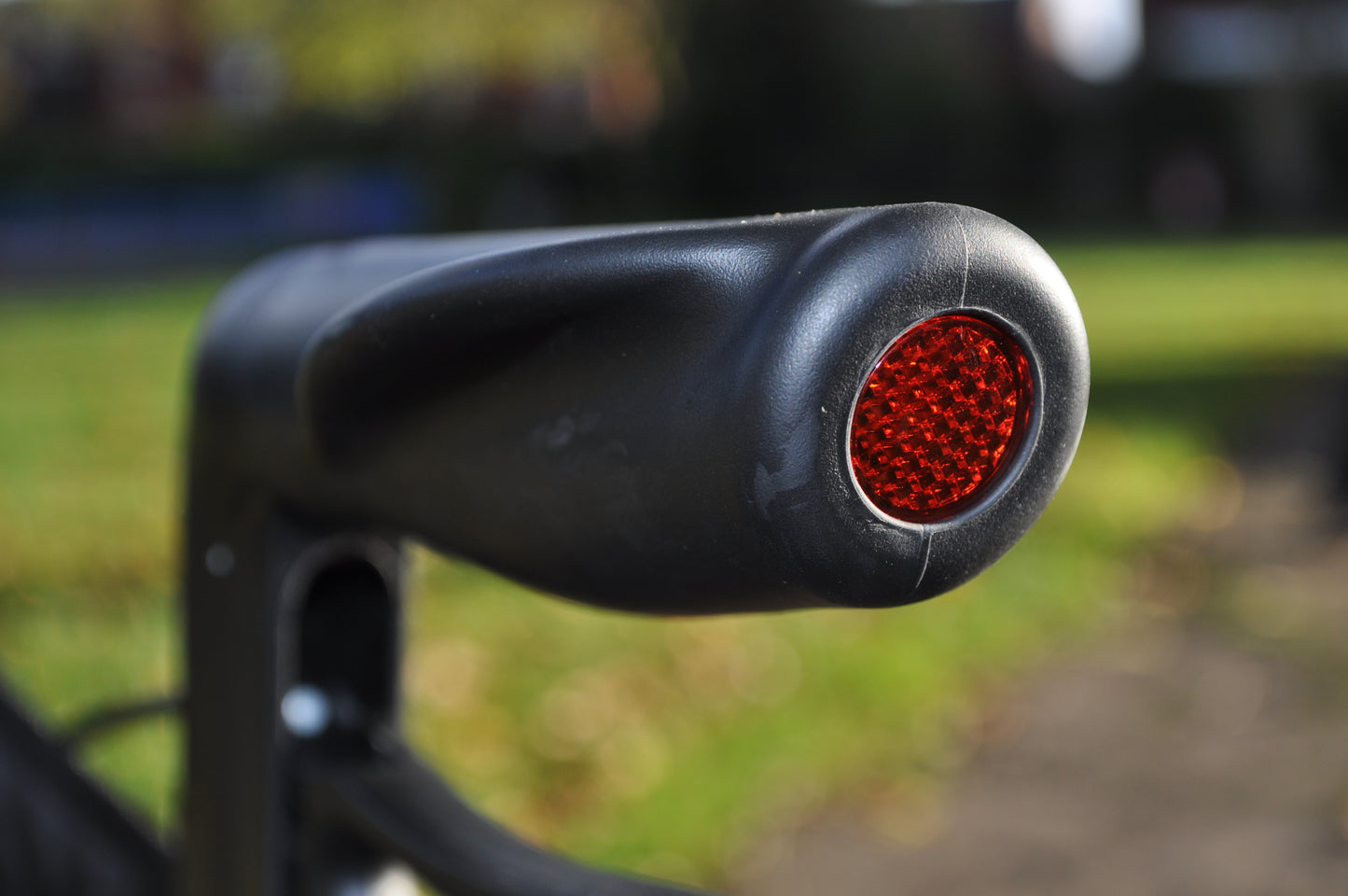 Close-up of Able2 Titan Carbon Rollator black handle with red reflector outdoors on blurred background