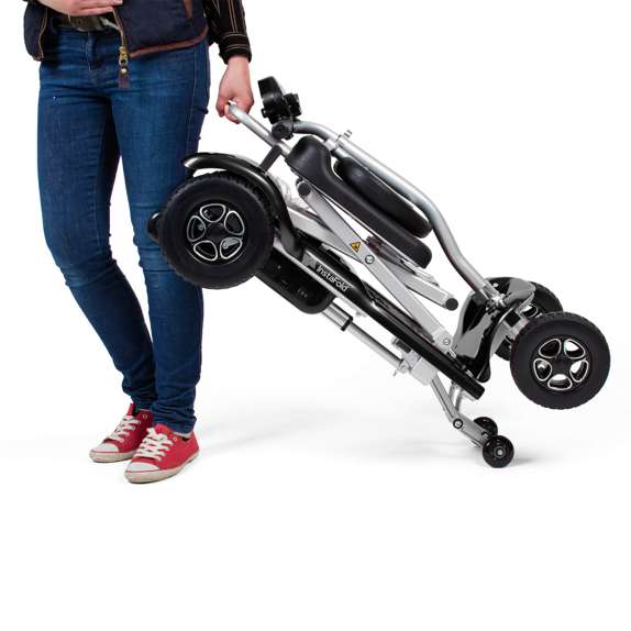 Person carrying the compact and folded Drive InstaFold automatic folding mobility scooter for easy portability.