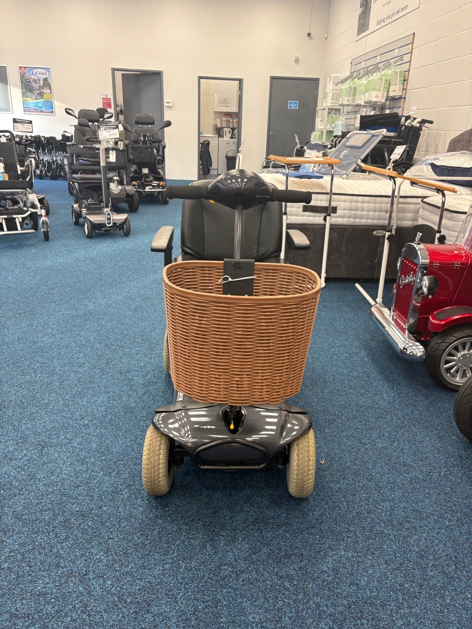 Refurbished Roma Paris Grey mobility scooter with front wicker basket displayed in showroom with other scooters and medical equipment.