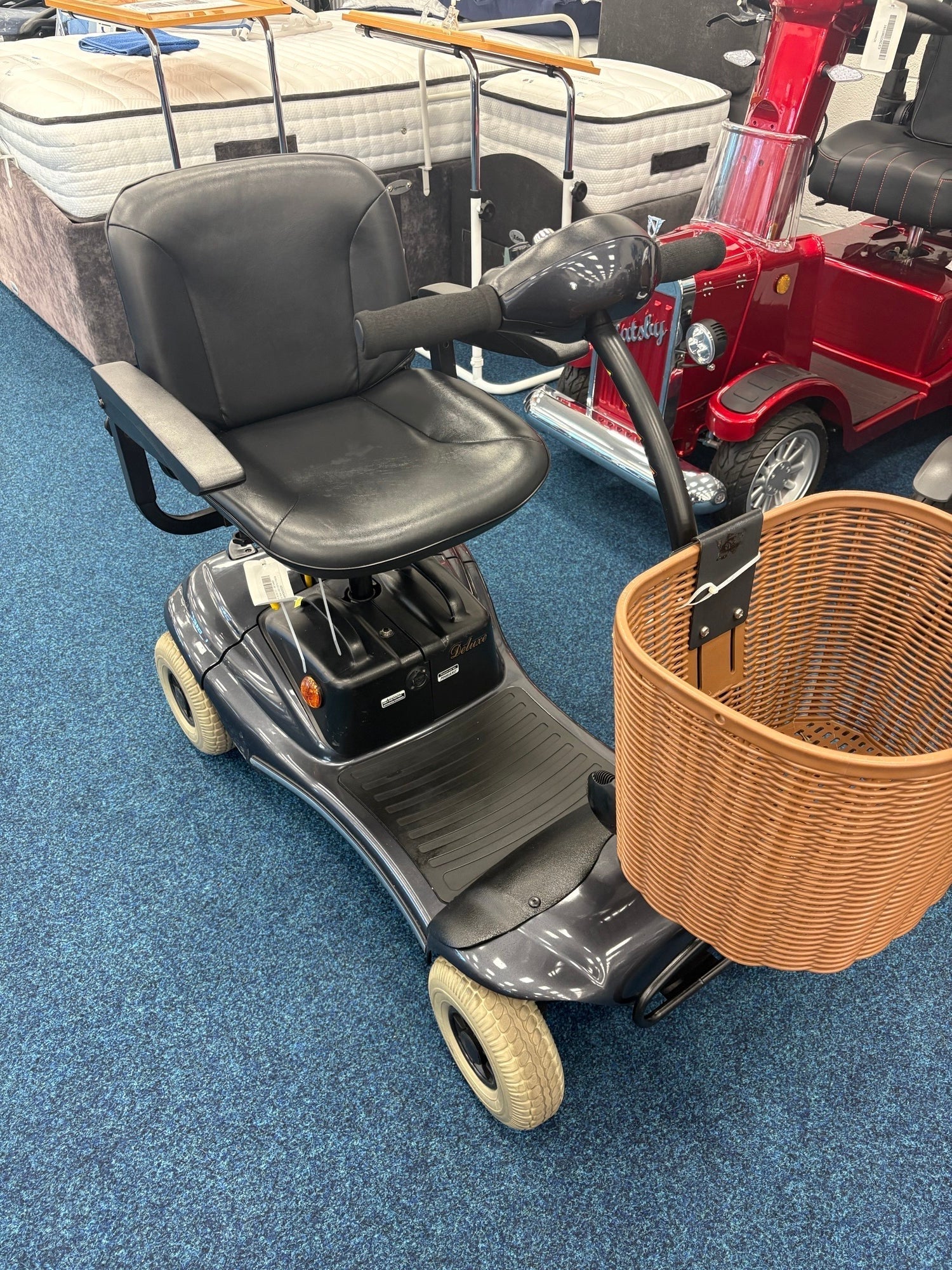 Grey Roma Paris mobility scooter with black seat and front wicker basket on blue carpet indoors
