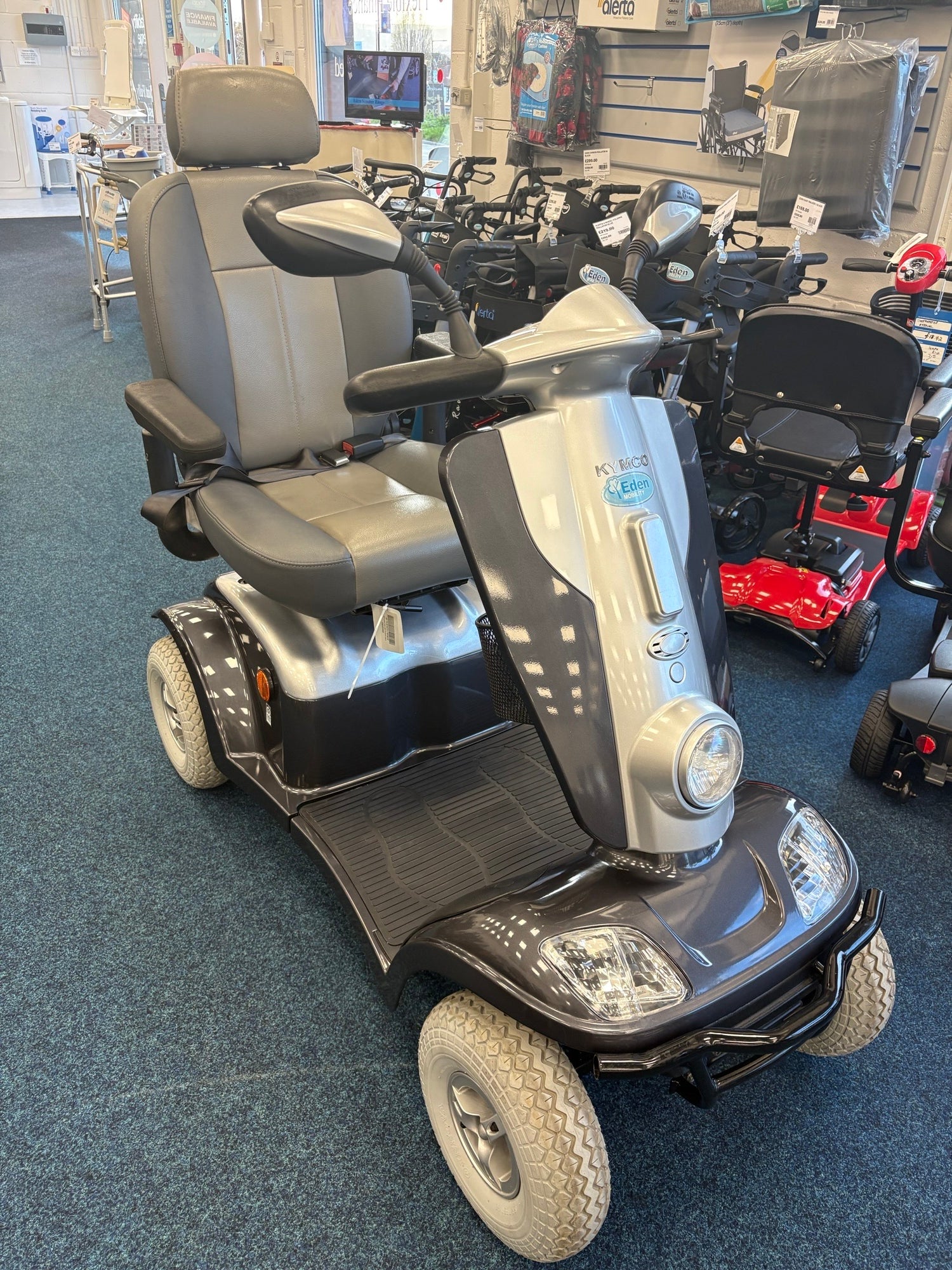 Grey Kymco Maxi XLS scooter with comfortable seat, rearview mirrors, and front headlight in a mobility store setting