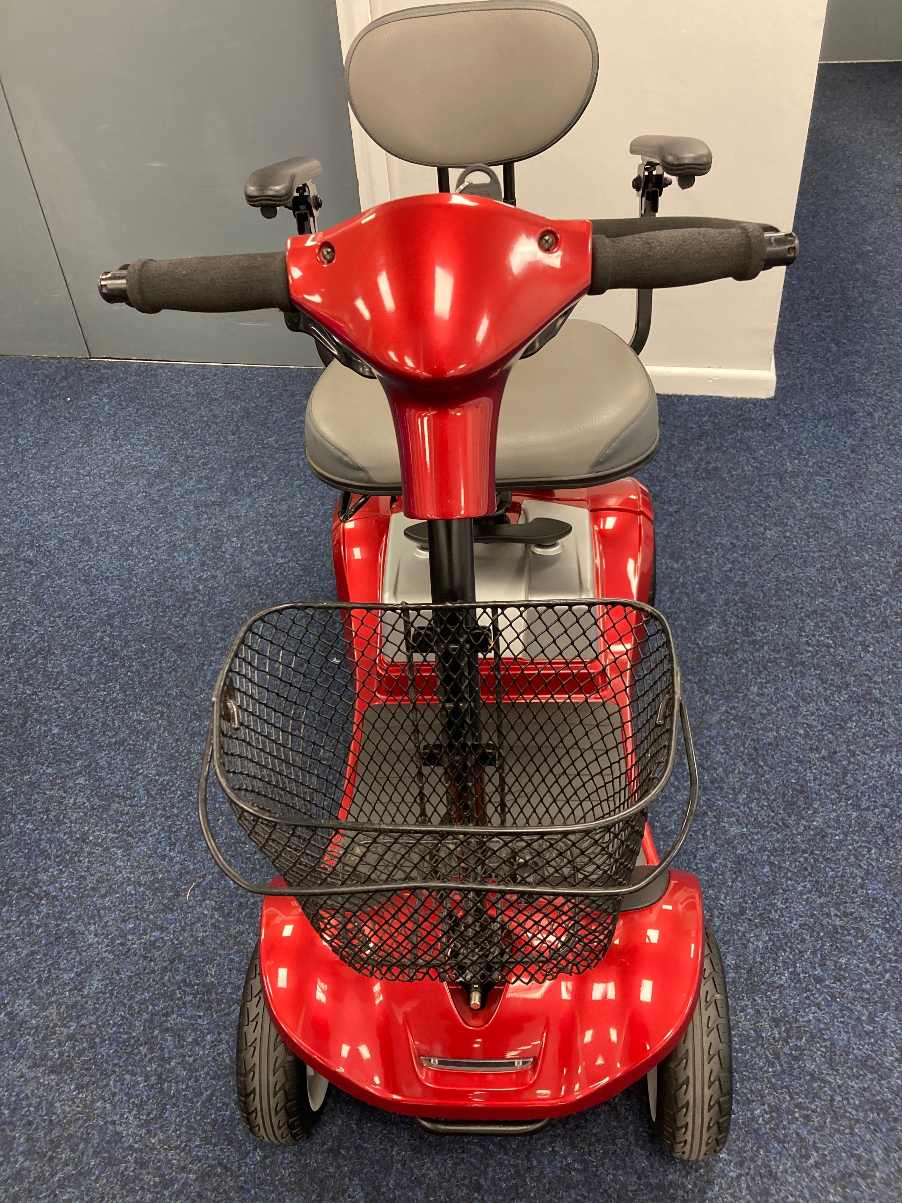 Front view of a fully refurbished red Kymco Mini Comfort mobility scooter with basket and padded seat on blue carpet