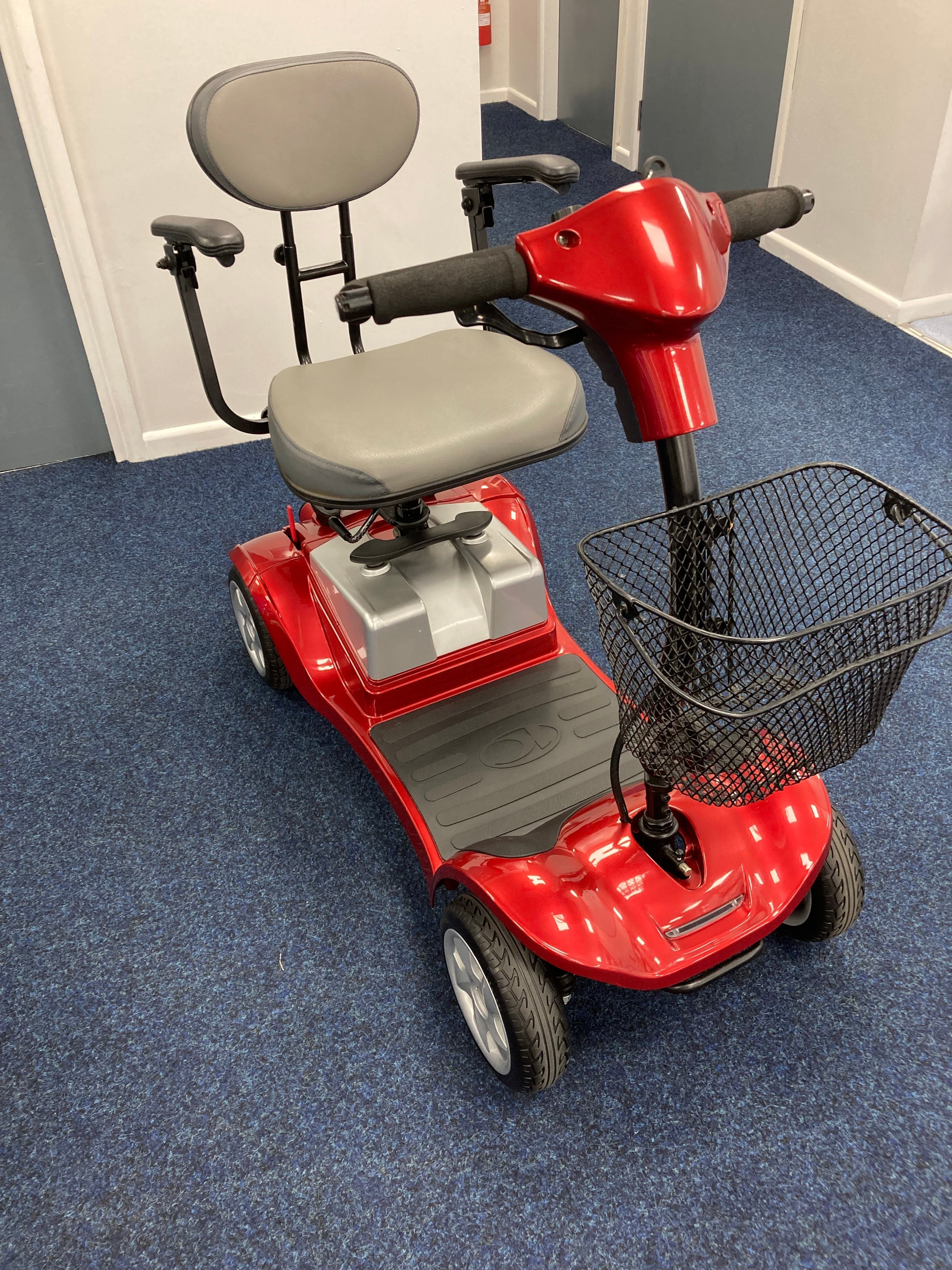 Red Kymco Mini Comfort mobility scooter with gray seat and front basket on blue carpet flooring indoors