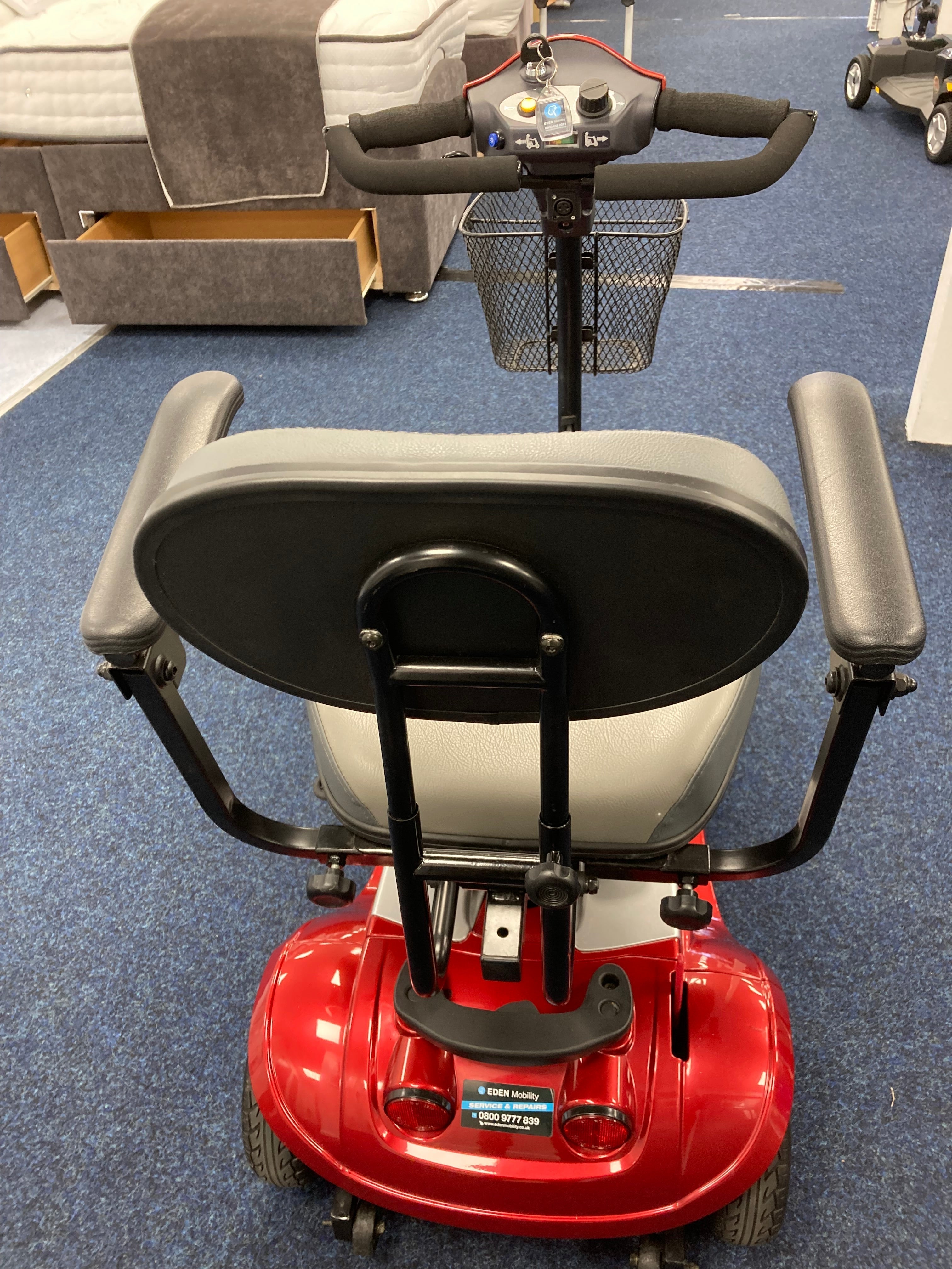 Rear view of a fully refurbished red Kymco Mini Comfort mobility scooter with padded seat and armrests on blue carpet.