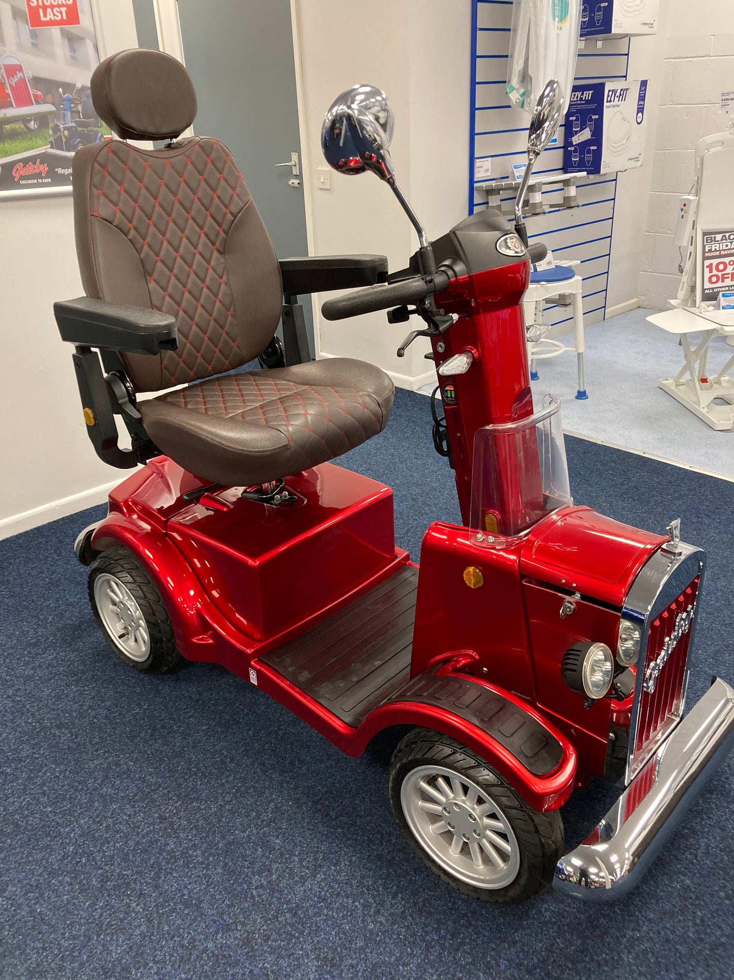 Red Eden Gatsby mobility scooter with brown cushioned seat and armrests displayed indoors on blue carpet