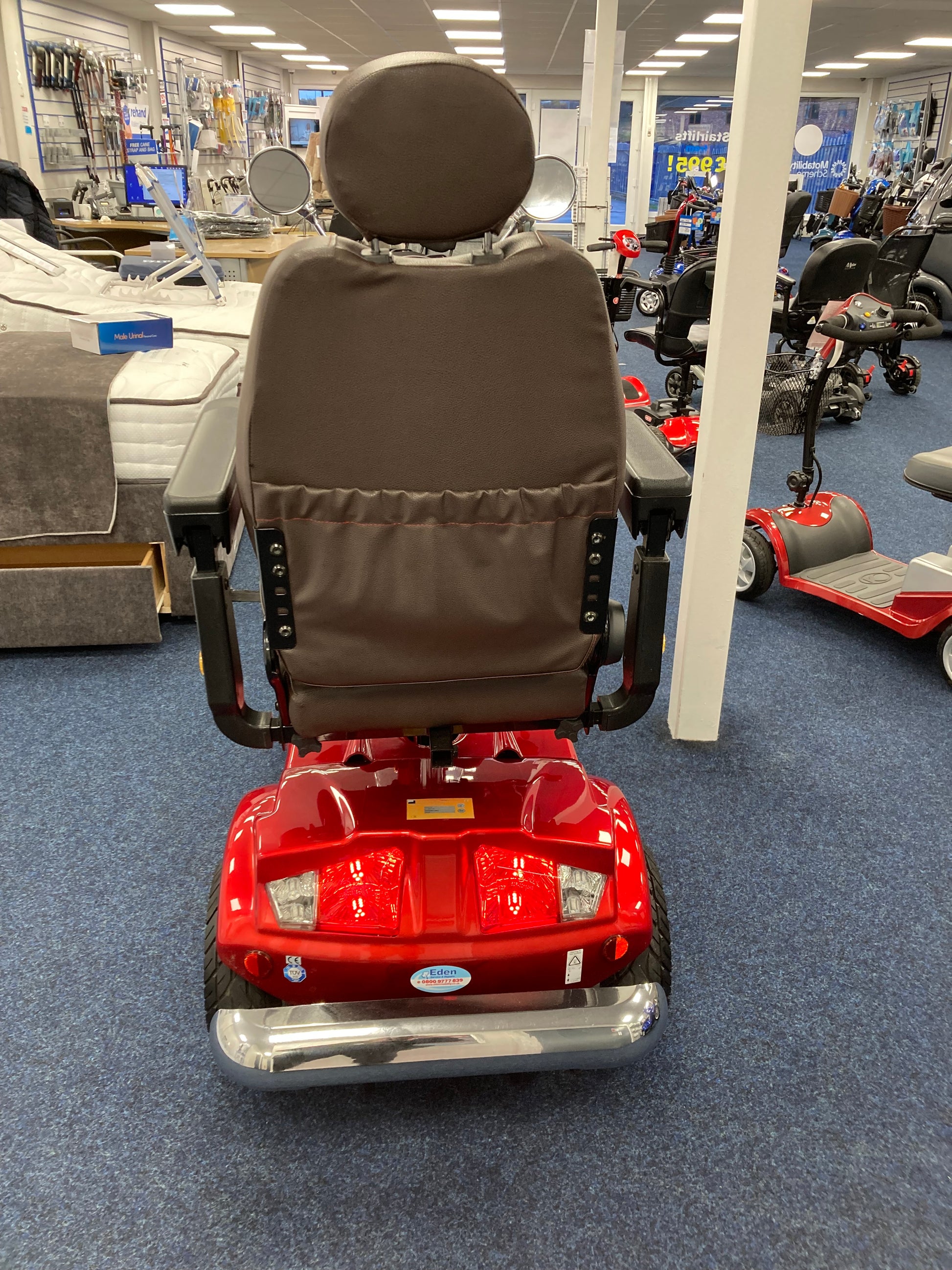 Rear view of red Eden Gatsby mobility scooter with brown seat inside mobility store on blue carpet floor