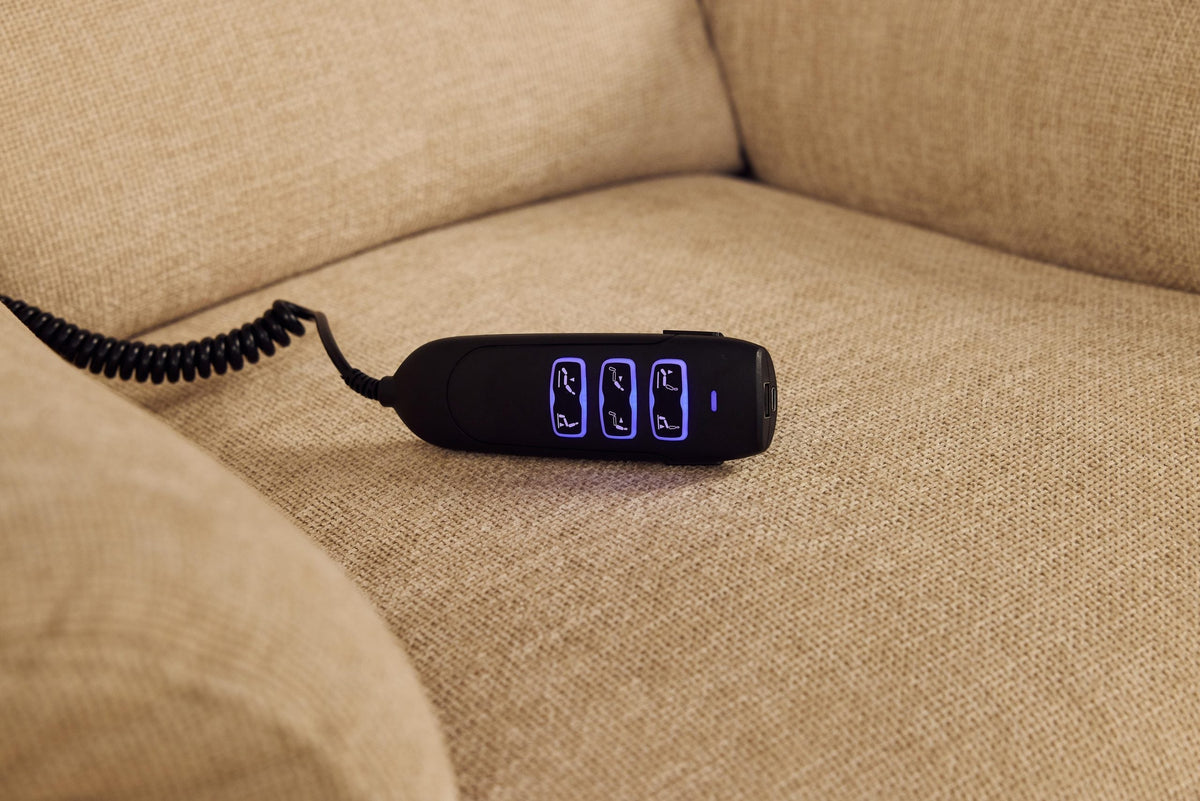 Close-up of black remote control with illuminated buttons resting on cream fabric of Sanford Rise and Recliner chair