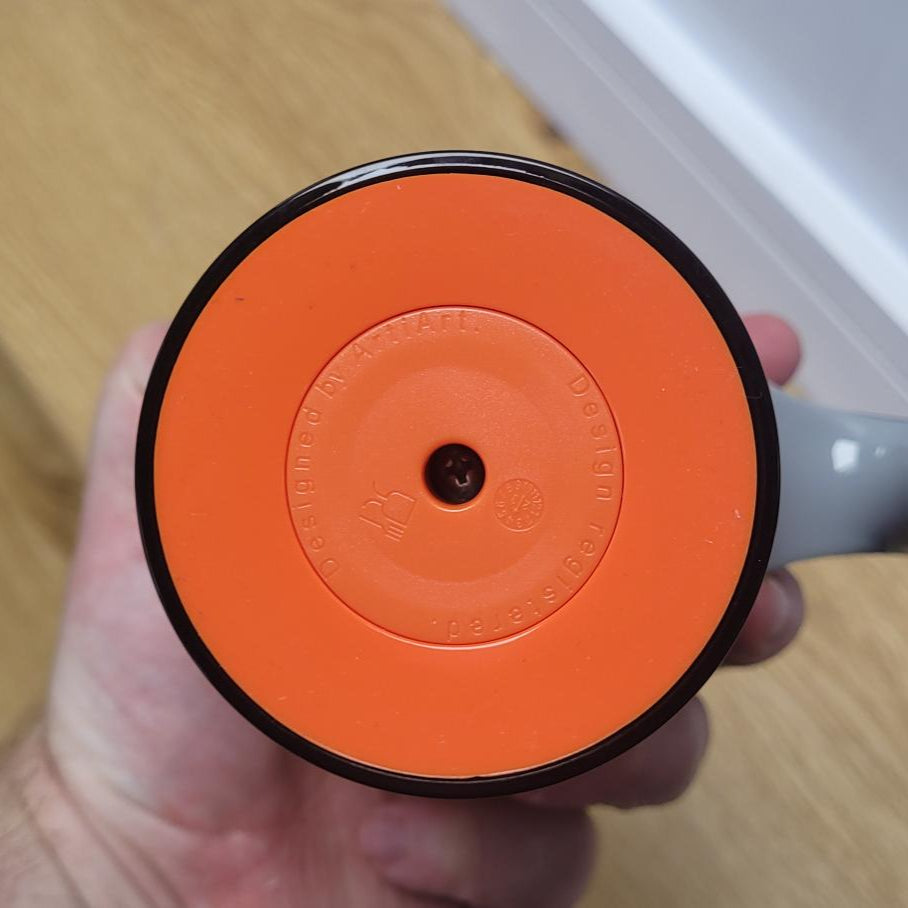 Hand holding an orange wheel with a gray handle on a wooden surface