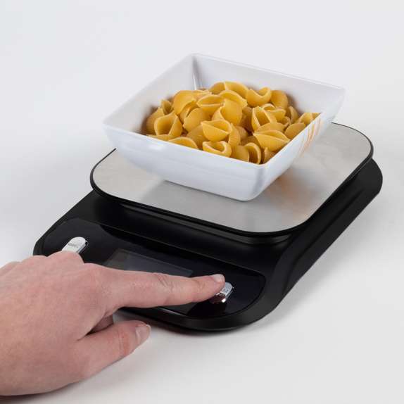 Black digital kitchen scale with a white bowl of pasta on a white background