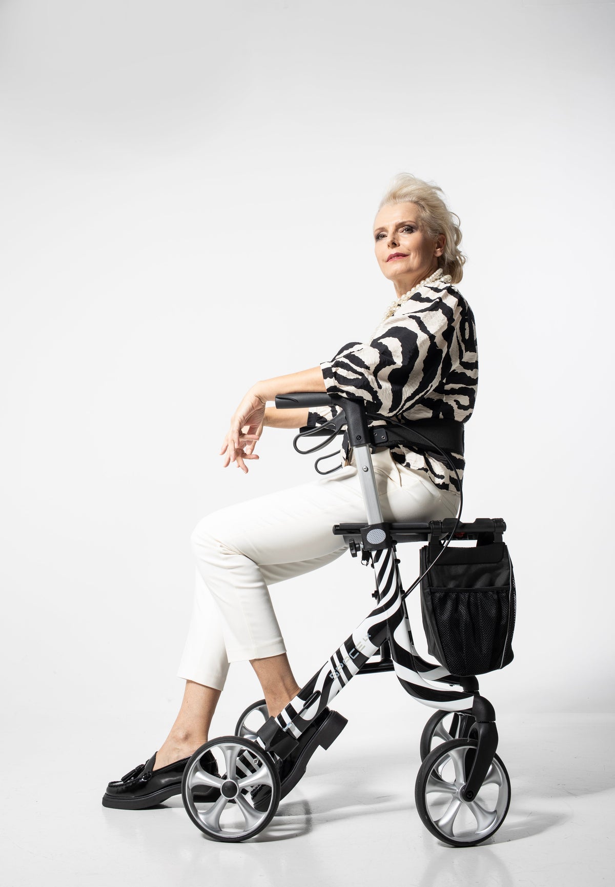 Senior woman demonstrating stylish, lightweight Space LX Art Line Rollator with zebra pattern and practical storage bag