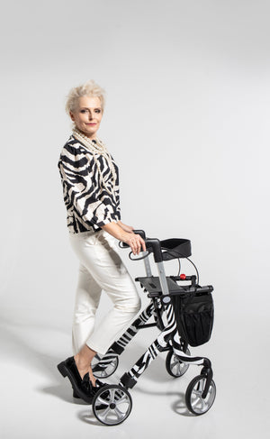 Elegant woman using a zebra-striped Space LX Art Line Rollator walking aid with black storage bag and comfortable hand grips