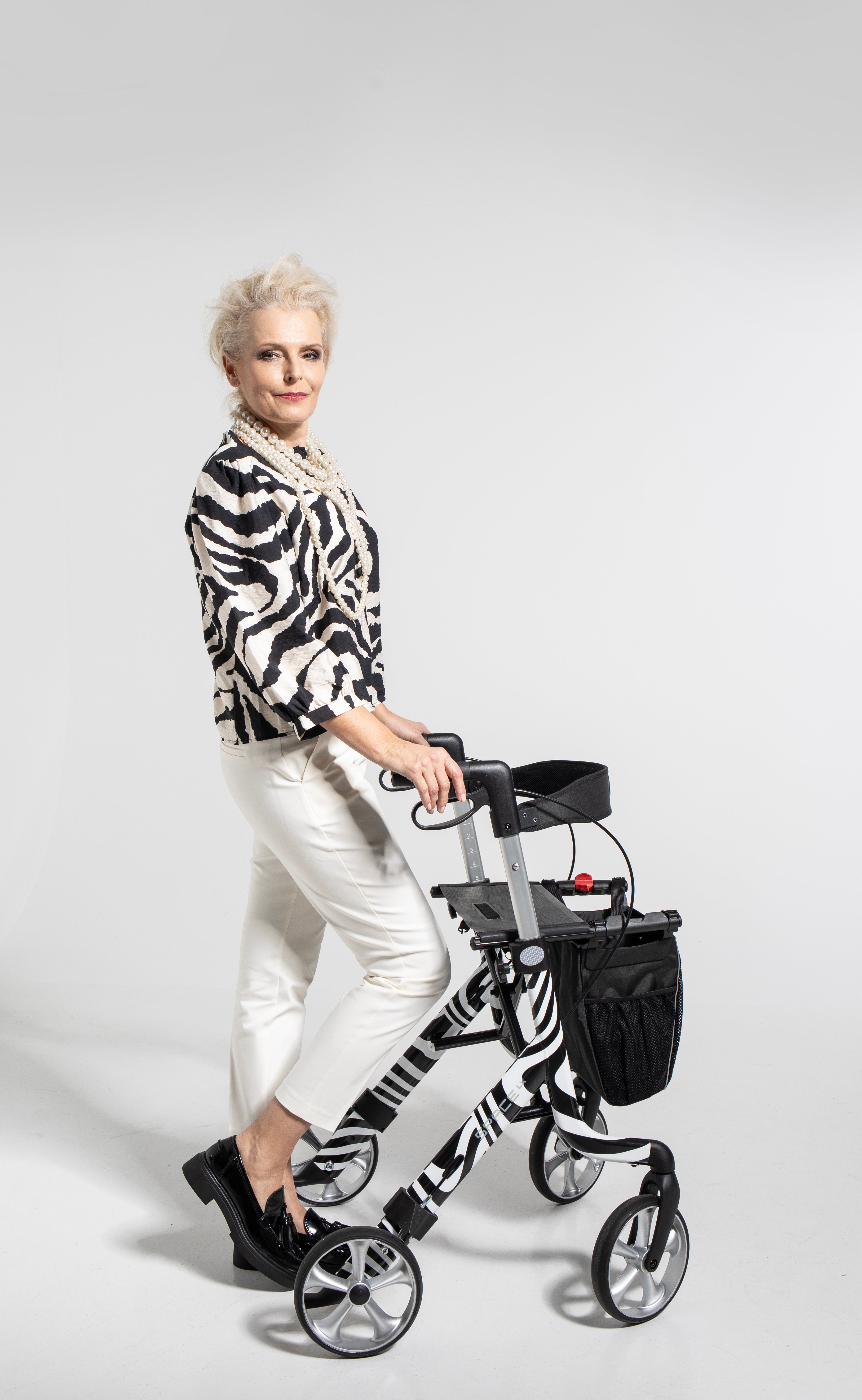 Elegant woman using a zebra-striped Space LX Art Line Rollator walking aid with black storage bag and comfortable hand grips