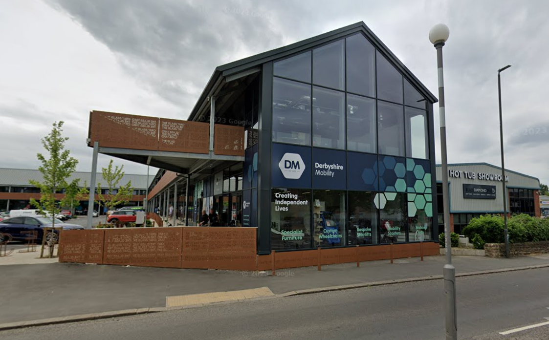 Modern building with large glass windows housing Derbyshire Mobility on a cloudy day with parked cars nearby